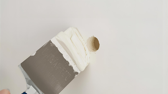 A person applying drywall compound to a hole in a white wall with a putty knife.