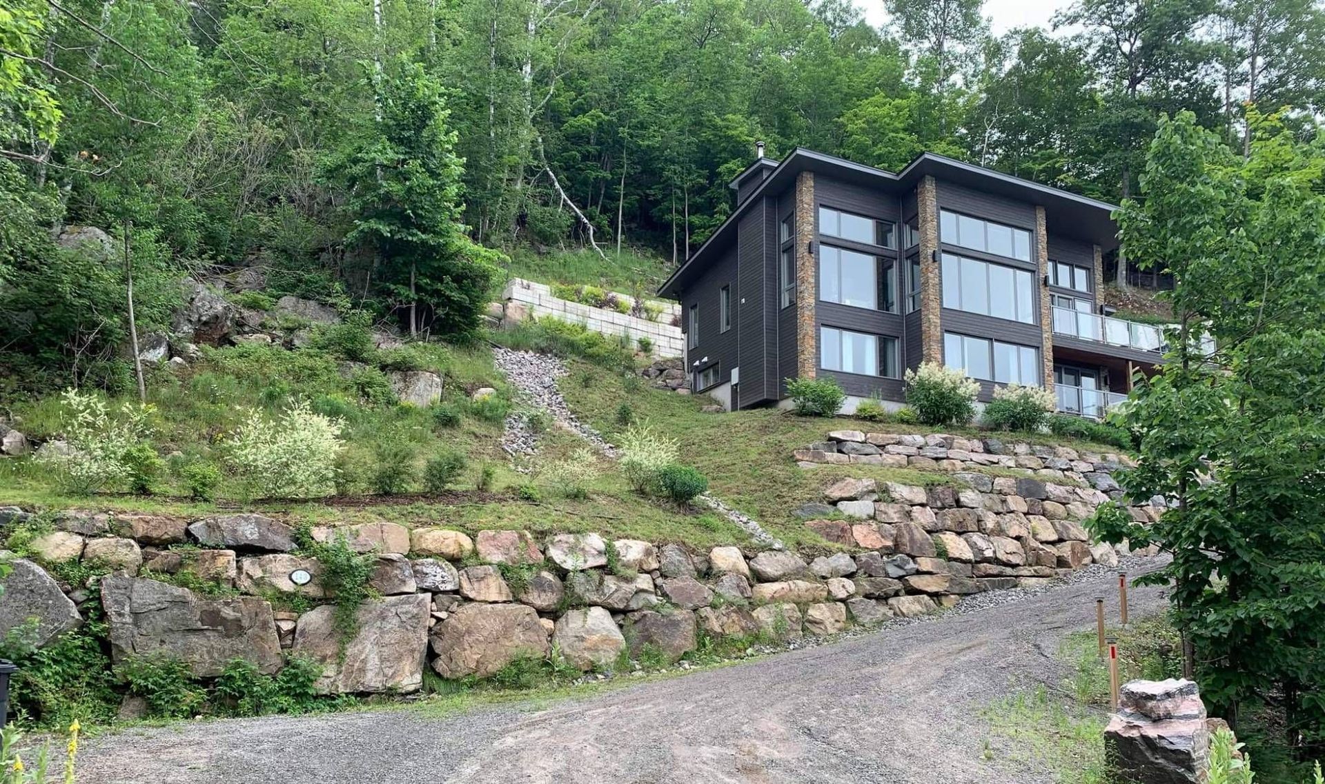 Une grande maison est située au sommet d'une colline entourée d'arbres.