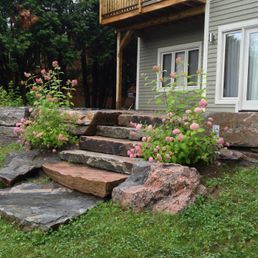 Une maison avec des escaliers faits de roches et de fleurs devant.