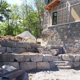 Un grand mur de pierre est en construction devant une maison.