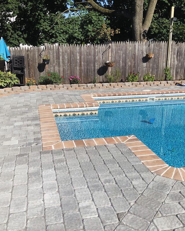 A large swimming pool surrounded by bricks and a wooden fence