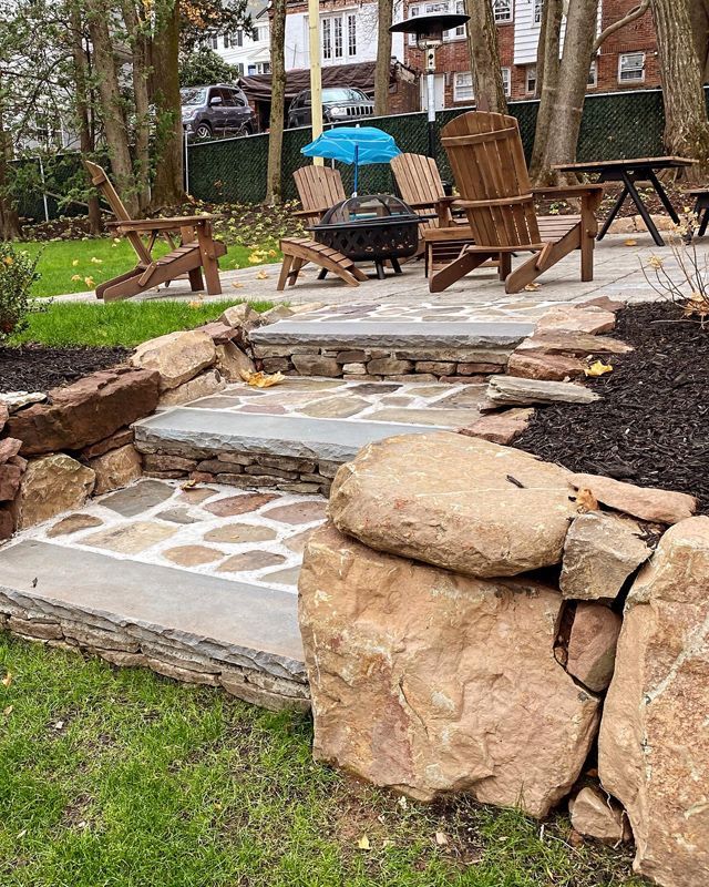 A patio with wooden chairs , a fire pit , and a blue umbrella.