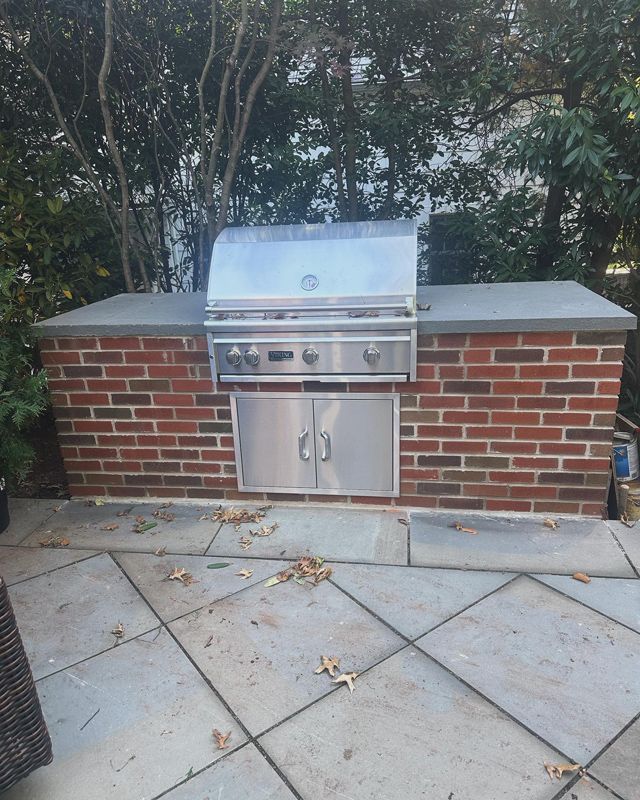 A grill is built into a brick wall on a patio