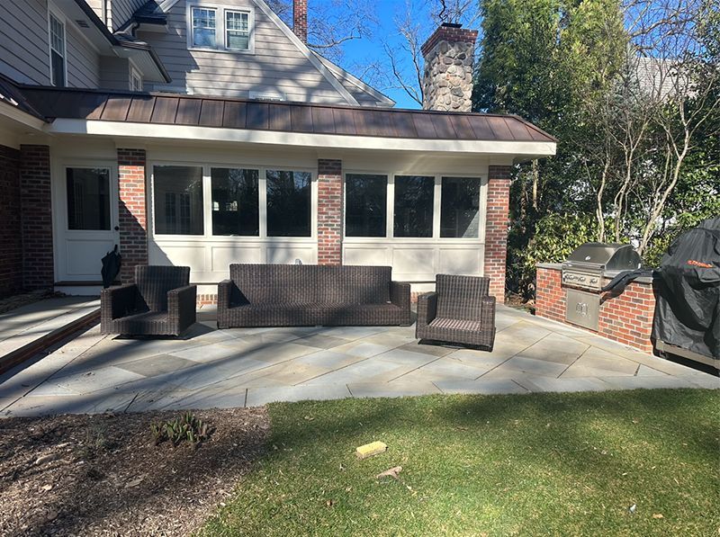 A patio with a couch and chairs in front of a house.