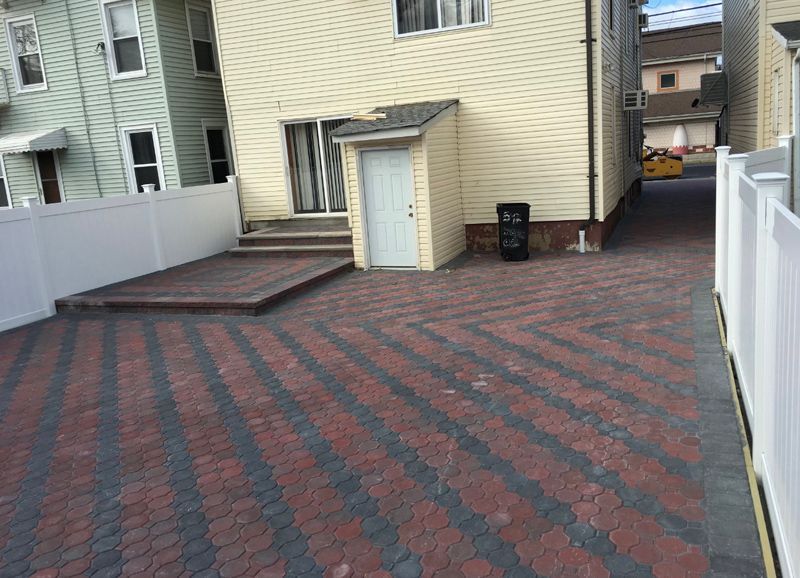 A brick driveway leading to a house with a white fence.
