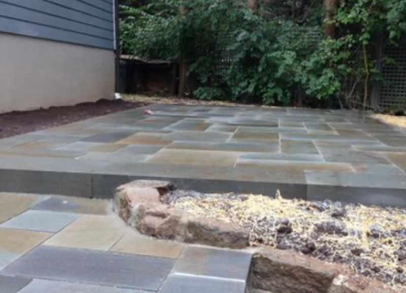 A patio with a rock in the middle of it and a house in the background.