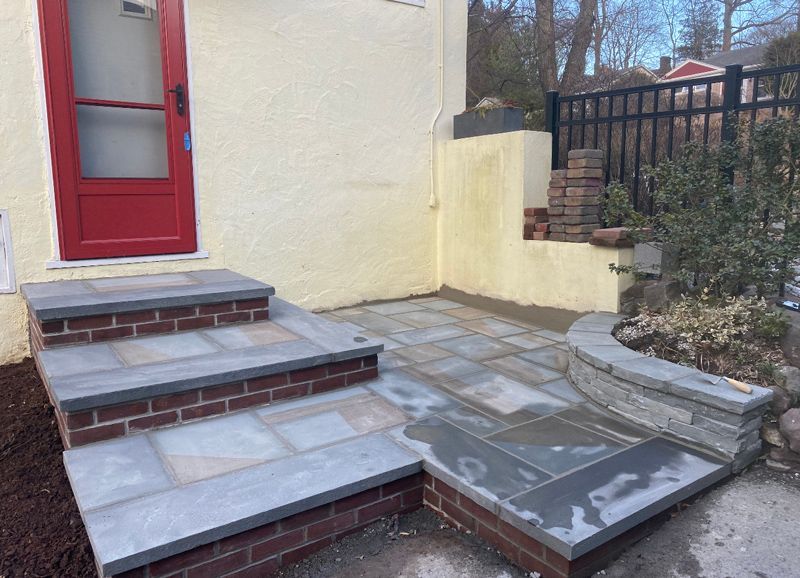 A brick walkway with stairs leading up to a red door.
