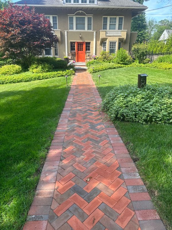 A brick walkway leading to a house with a red door