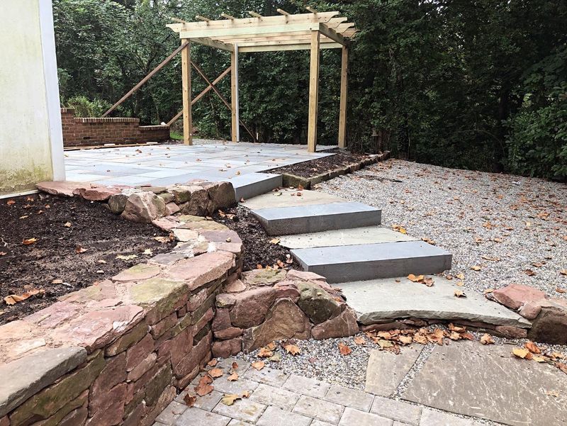 A patio with a pergola and steps leading to it.