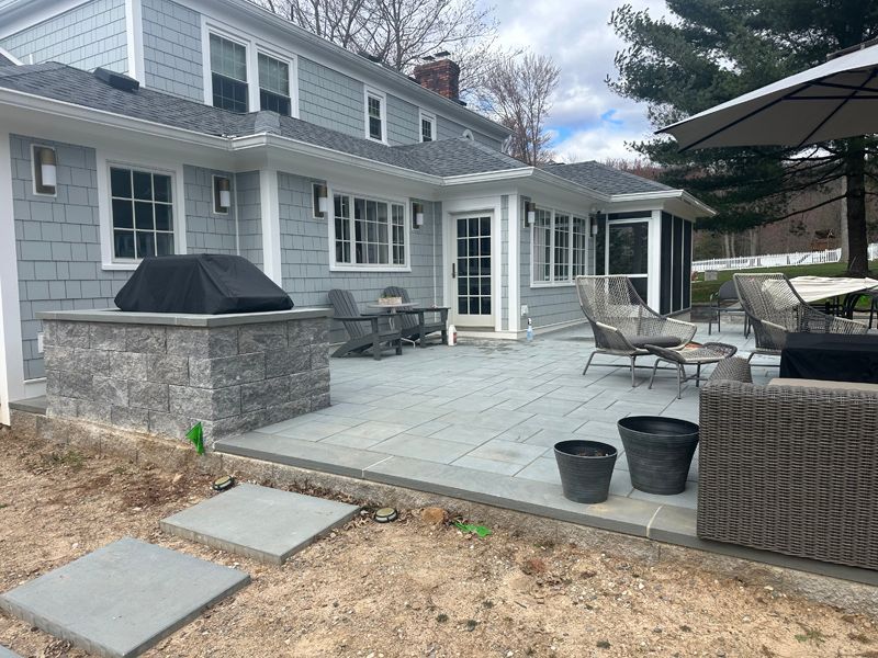 A patio with a grill and chairs in front of a house.