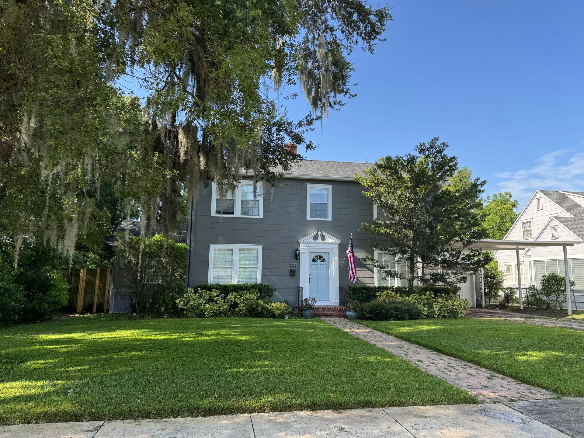 Two-story gray house with light blue door, American flag, sidewalk, and green lawn.