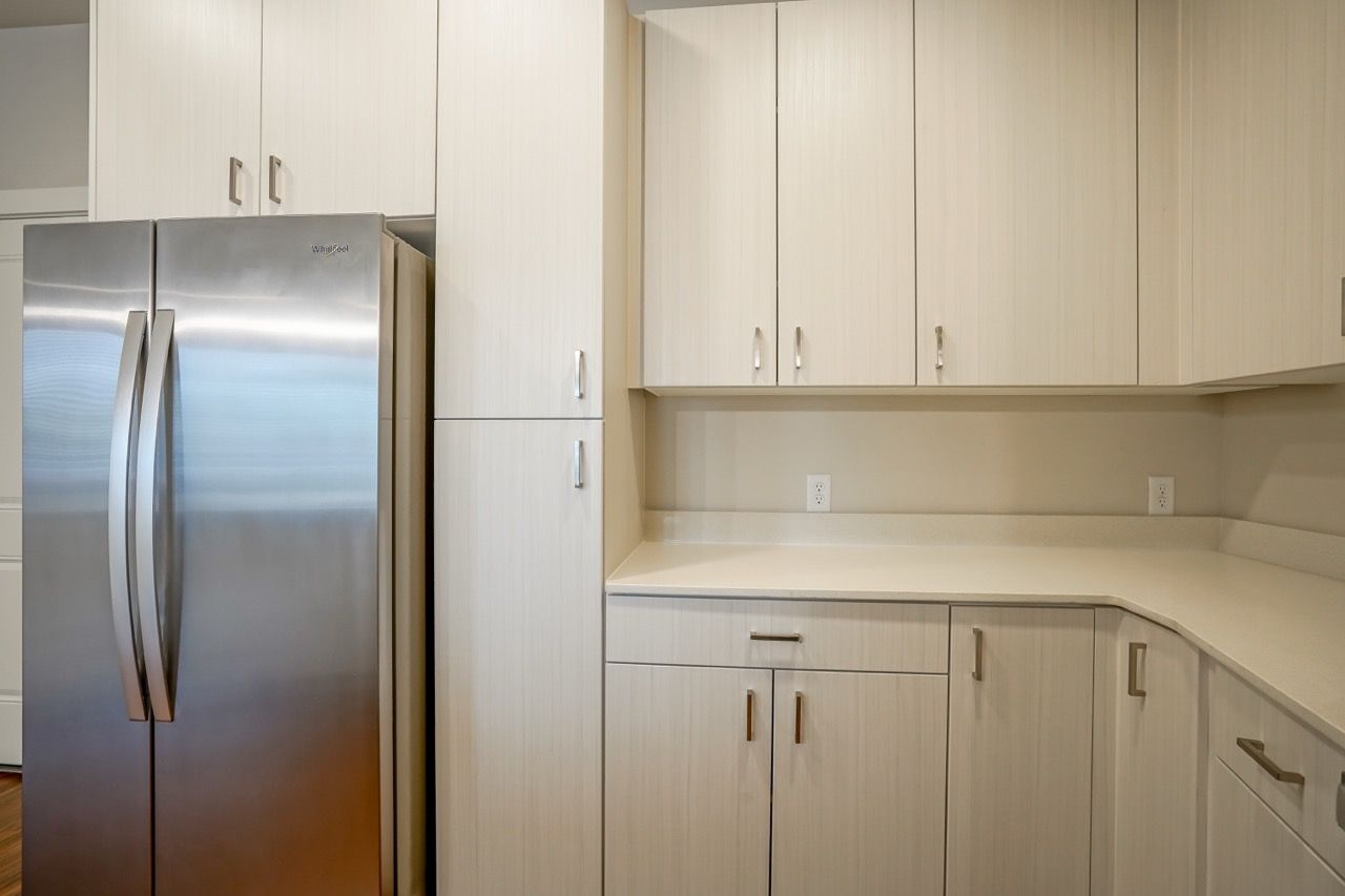 Interior view of a modern kitchen with white cabinets and a stainless steel refrigerator.