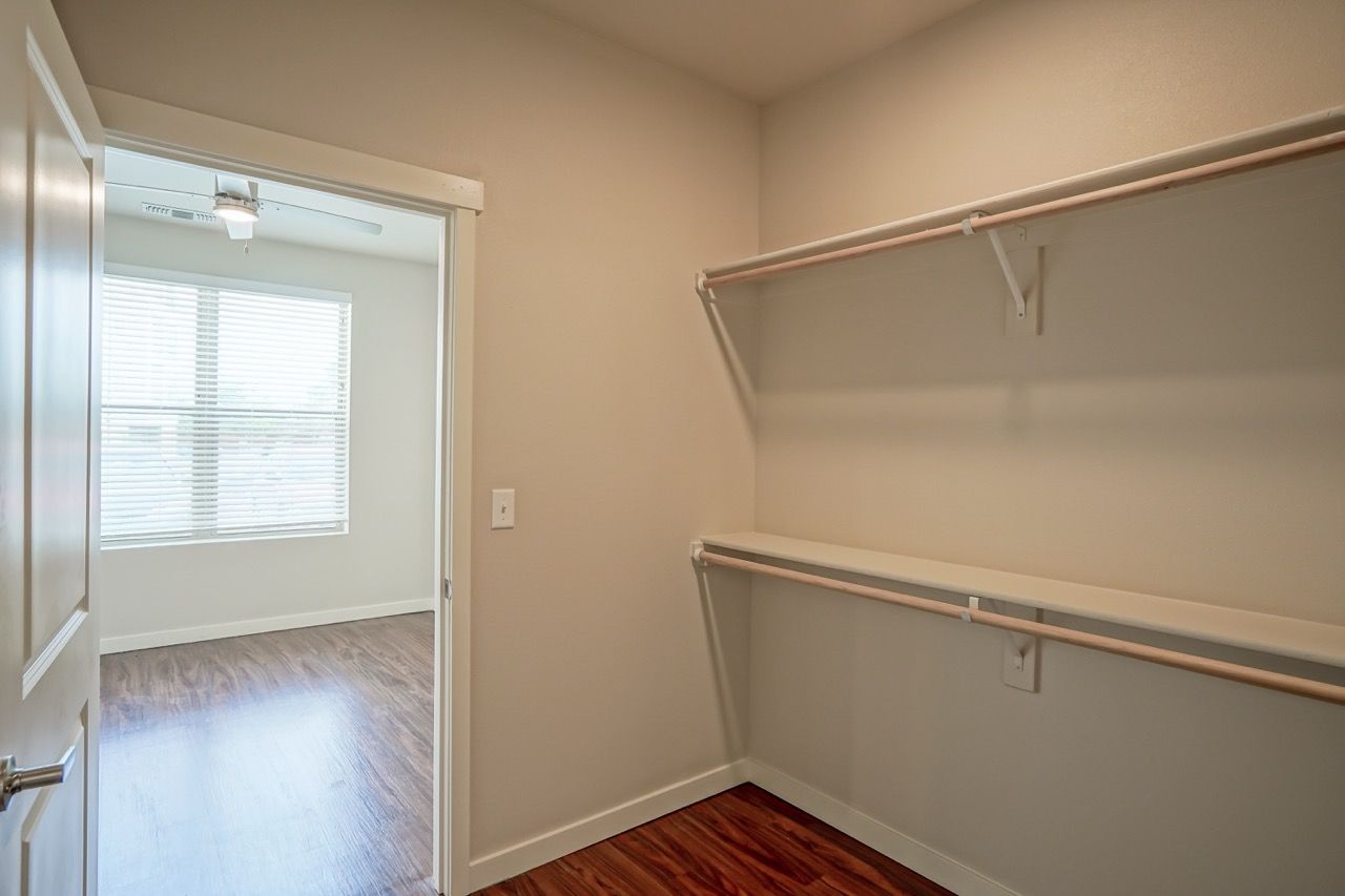 Walk-in closet with two hanging rods, shelf, and wood floor.