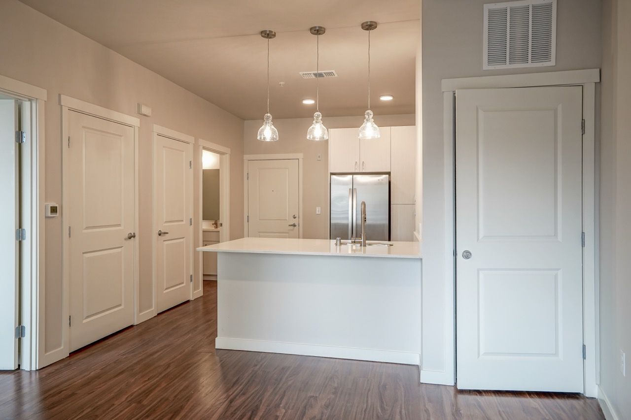 Open-concept kitchen with an island, white cabinets, stainless steel refrigerator, and wood-style flooring.
