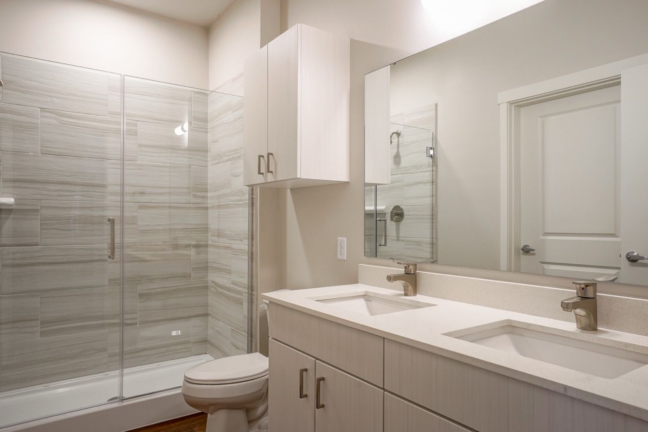 Modern bathroom with glass-enclosed shower, double sink vanity, and white cabinetry.