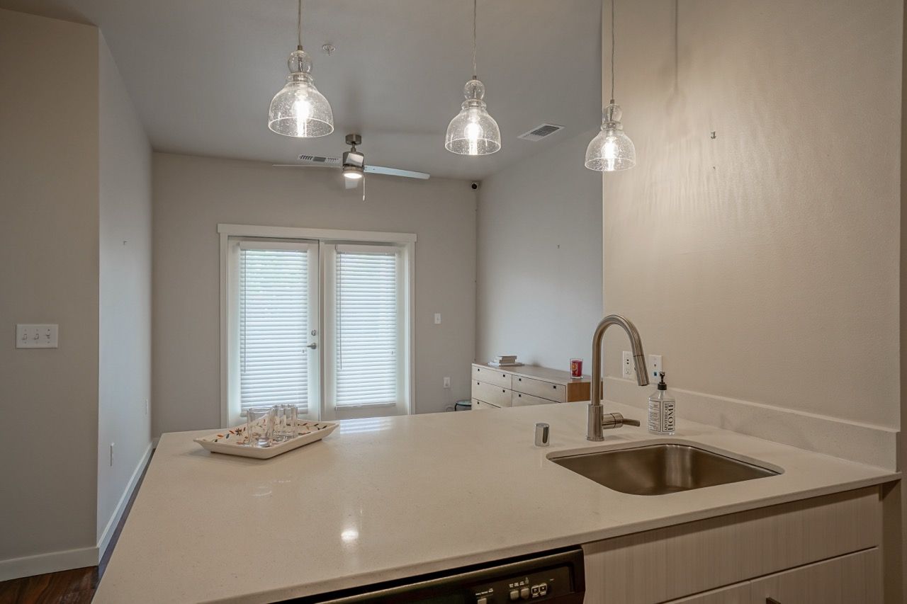 Kitchen with island, sink, pendant lights, and French doors with blinds in the background.