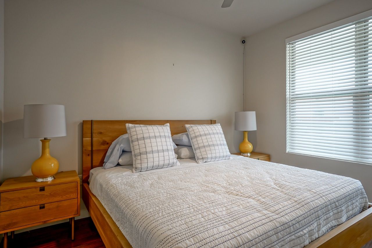 Bedroom with a wooden bed frame, two nightstands, white bedding, and a window with blinds.