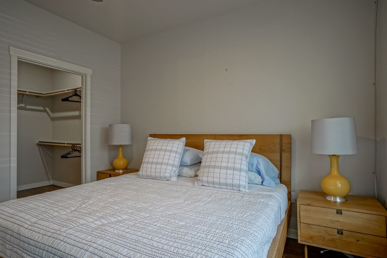 Bedroom with a wooden bed, two nightstands, yellow lamps, and an open closet on the left.