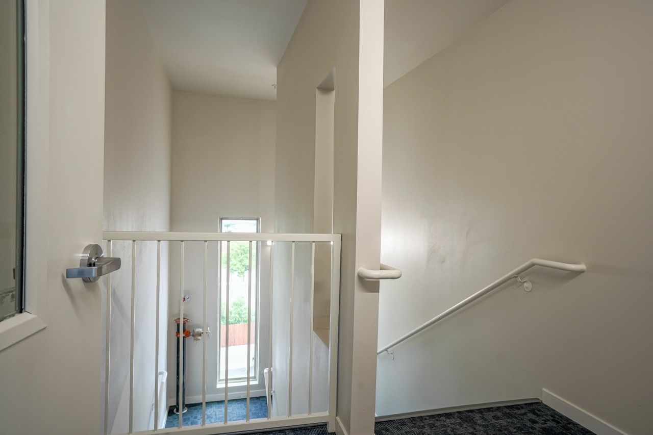 Indoor stairwell with white walls, metal railing, and a small window at the bottom of the stairs.