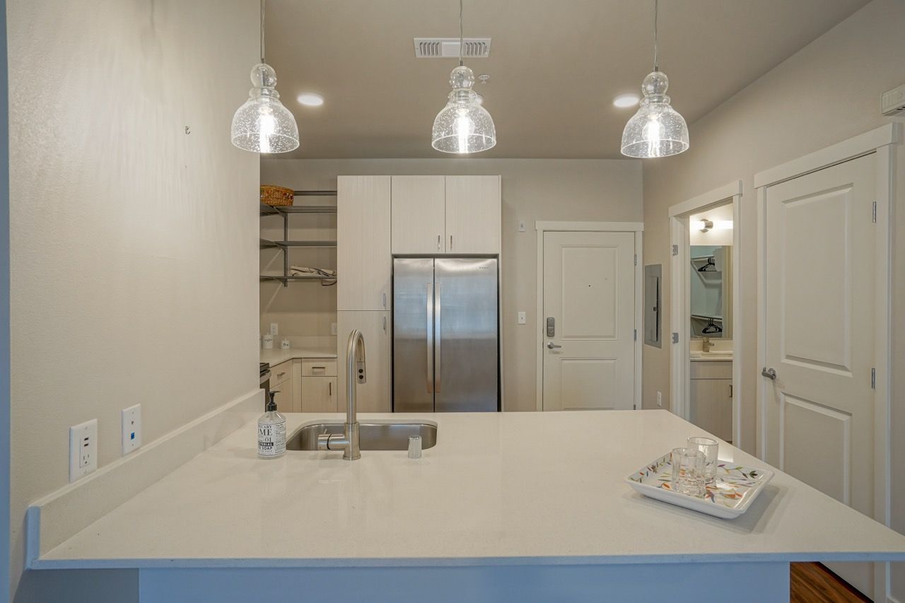 Modern kitchen with an island, stainless steel fridge, white cabinets, and glass pendant lights.