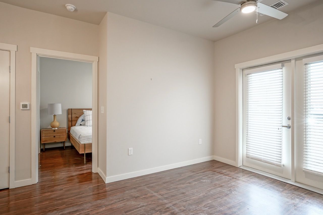 Living area with wood floors, ceiling fan, and balcony doors; doorway to a bedroom.