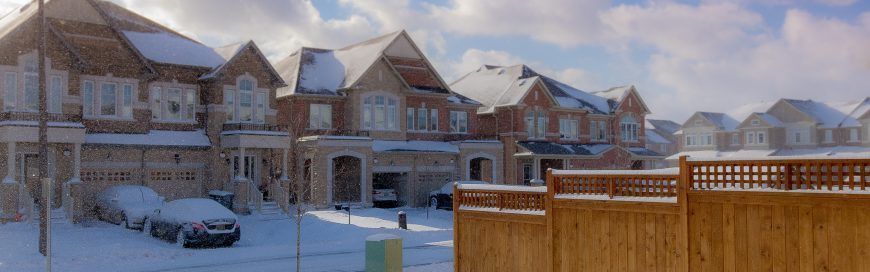 A row of houses covered in snow with a wooden fence in the foreground.
