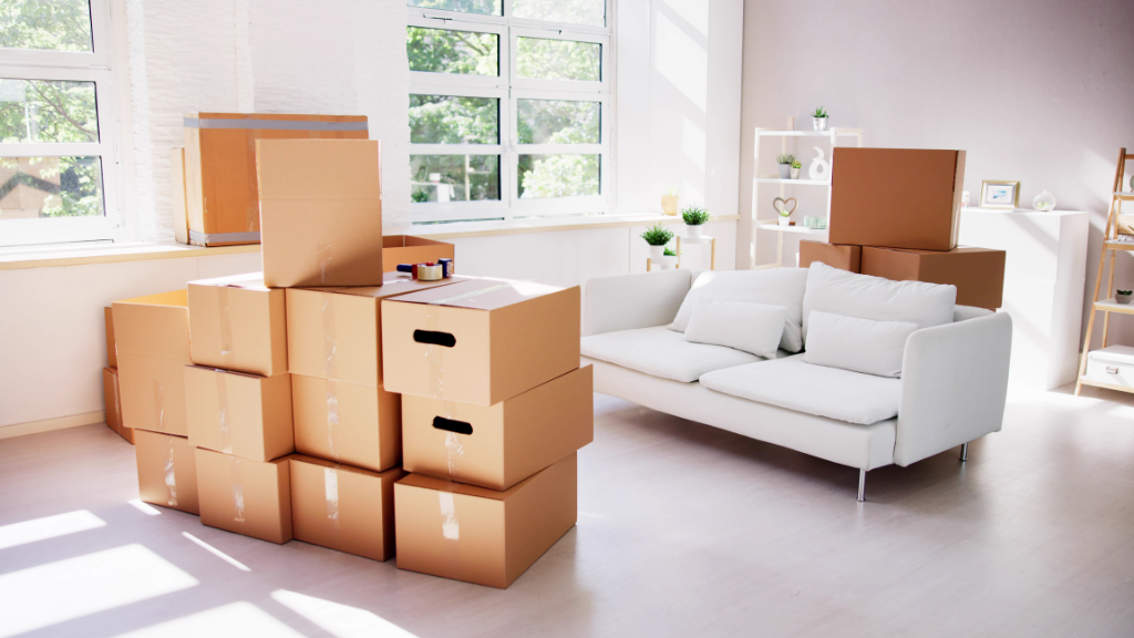 Three people unpacking cardboard boxes in a new, white-walled home; smiling and talking.