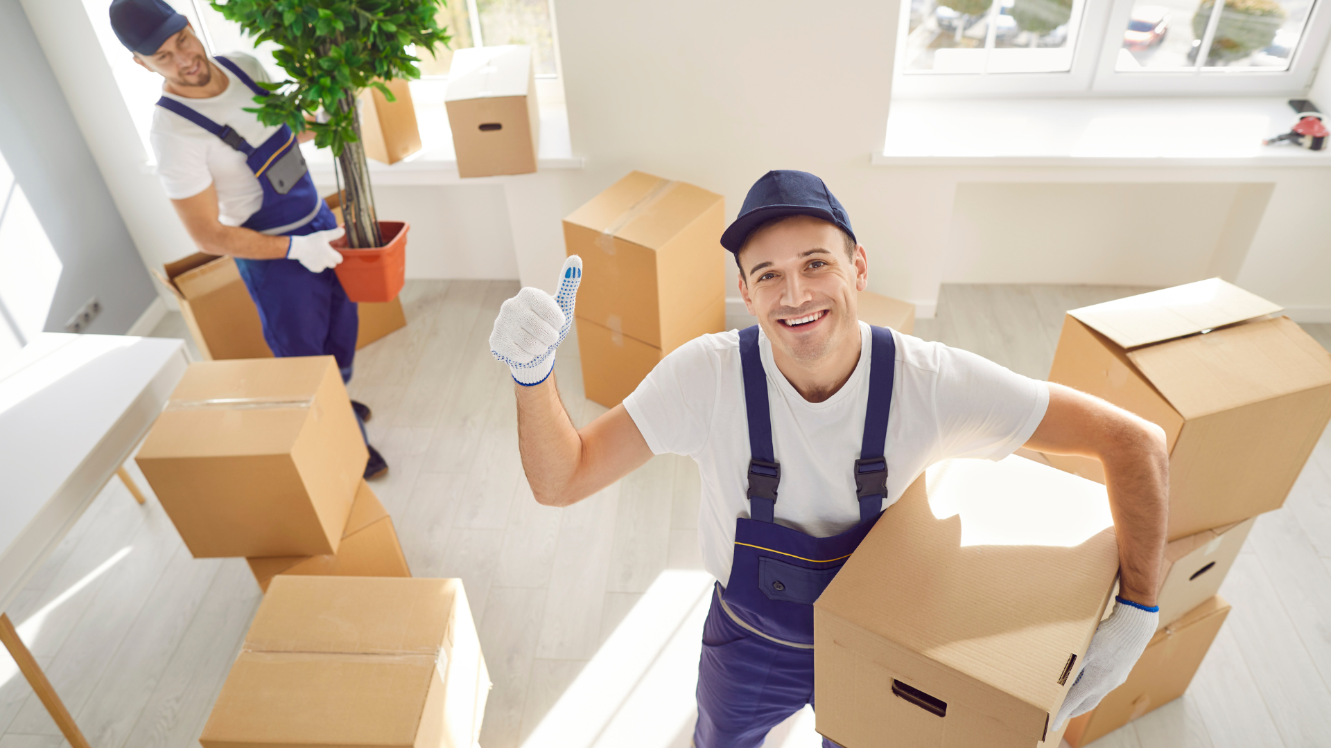 A man is holding a cardboard box and giving a thumbs up.