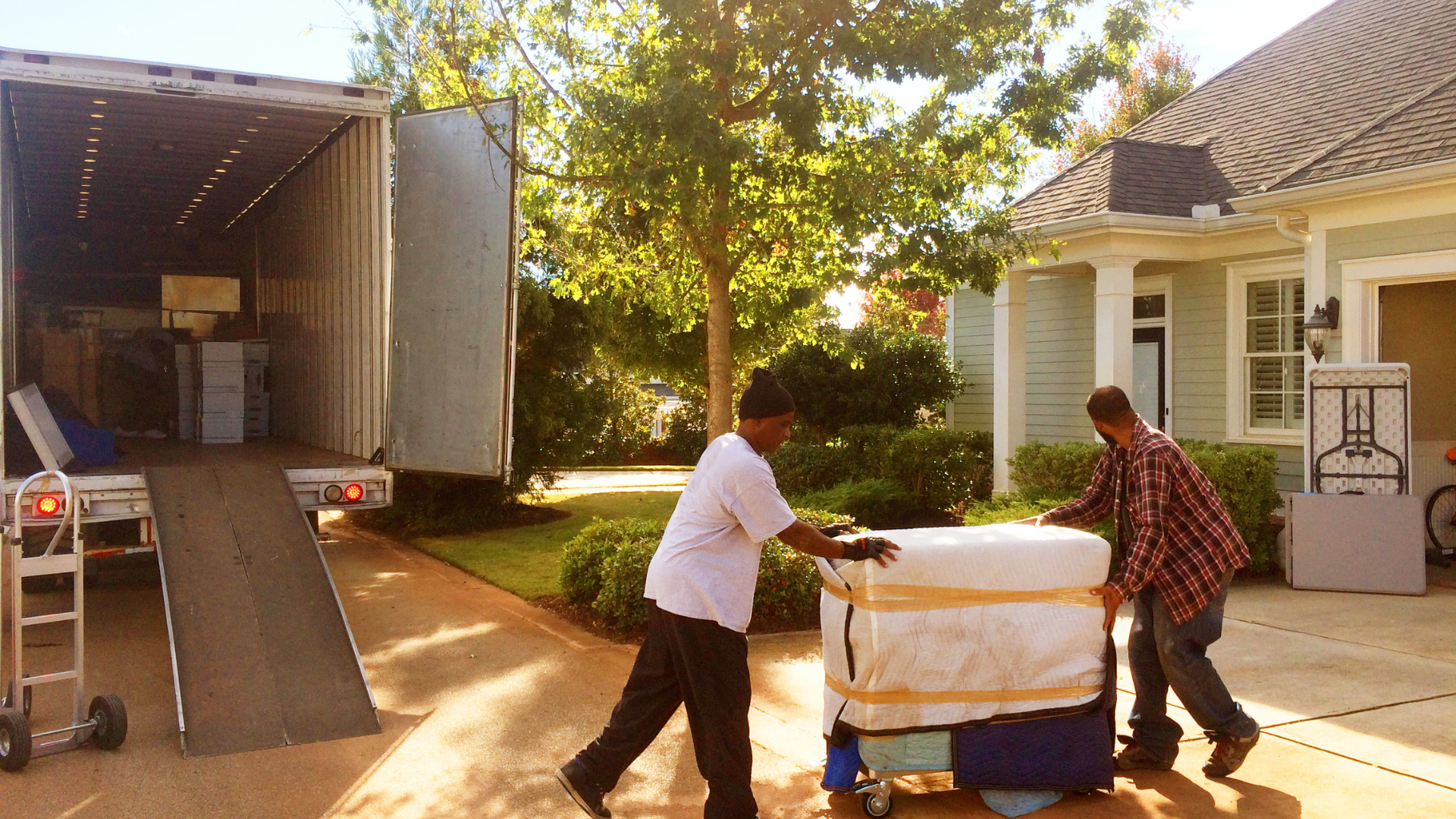 Two men are pushing a large item on a dolly in front of a house.