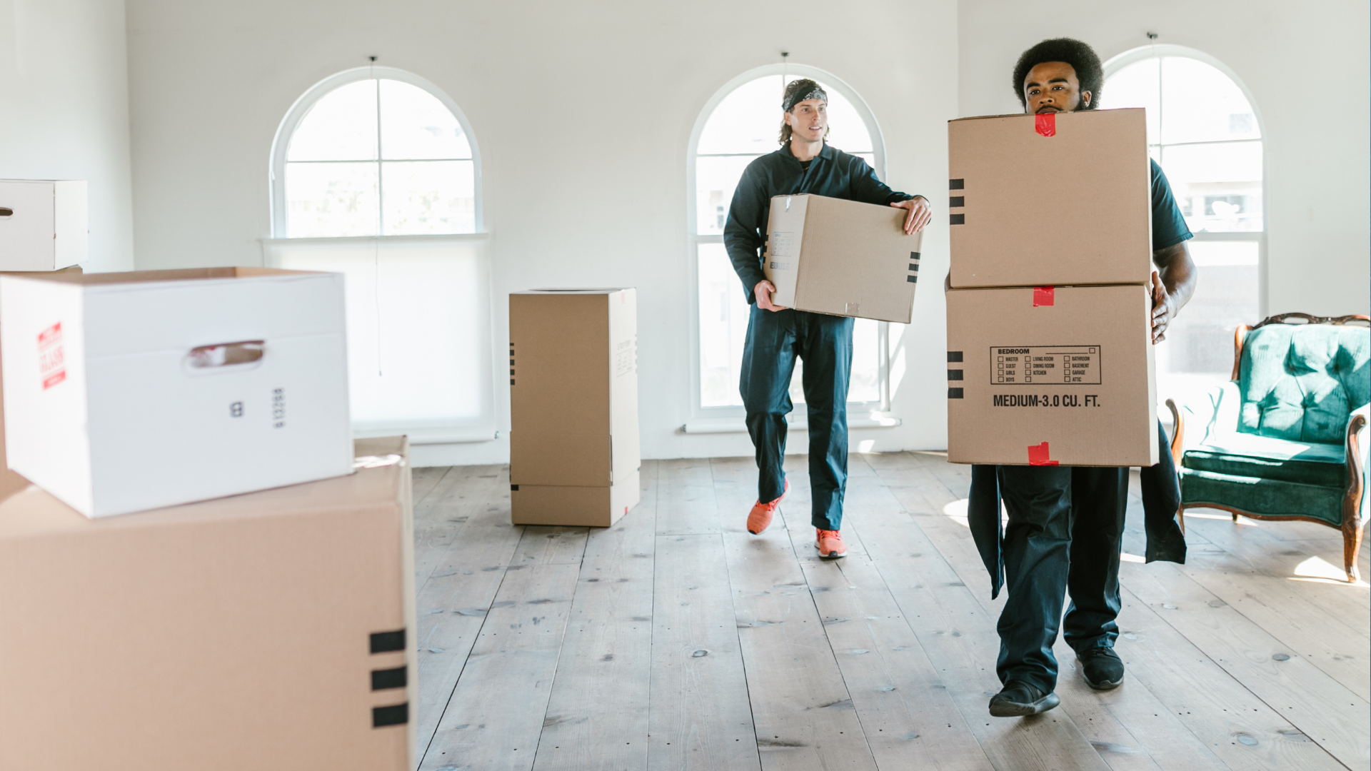 A man and a woman are carrying boxes in a room.