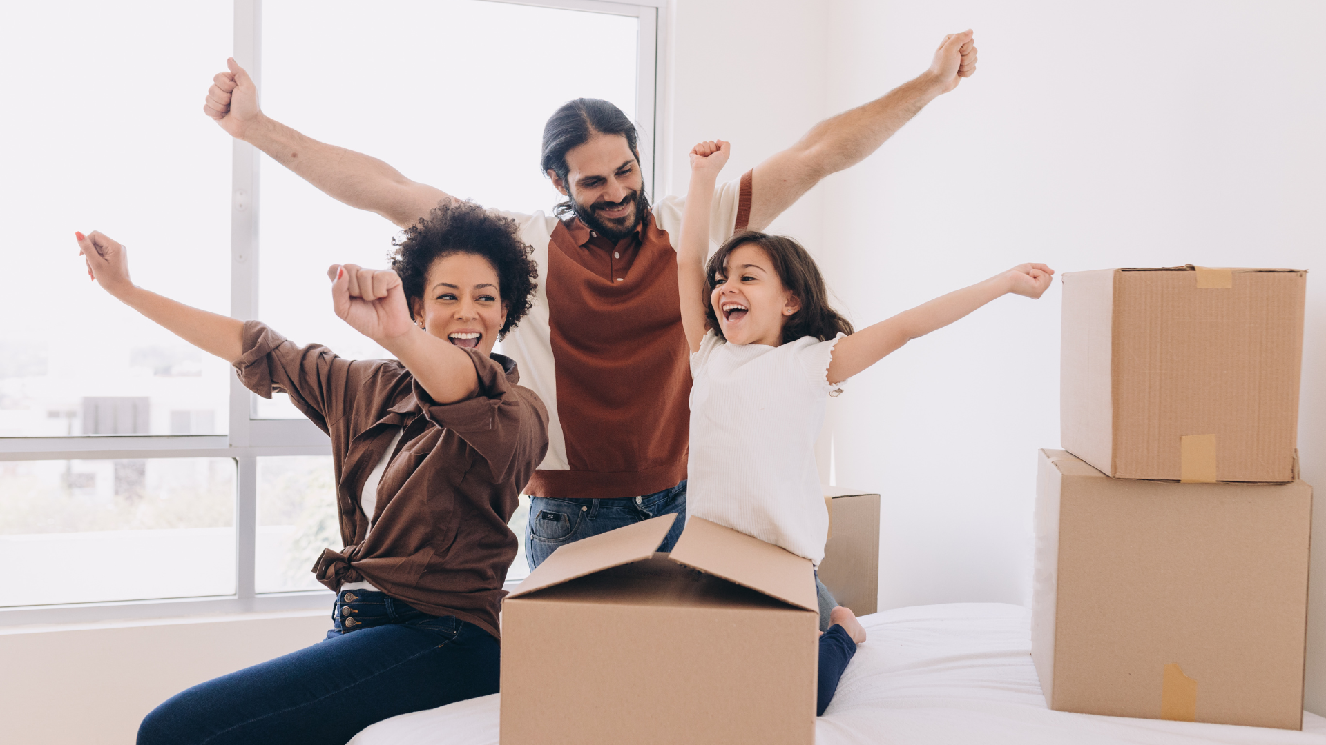 A family is sitting on a bed with their arms in the air.