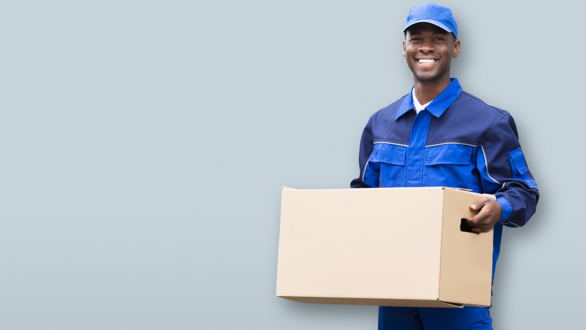 A delivery man in a blue uniform is holding a cardboard box.
