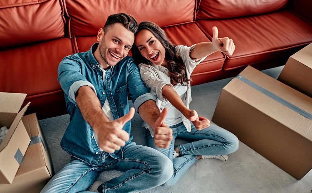 A man and a woman are sitting on the floor giving a thumbs up.