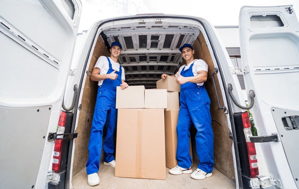 Two movers are standing in the back of a van filled with boxes.