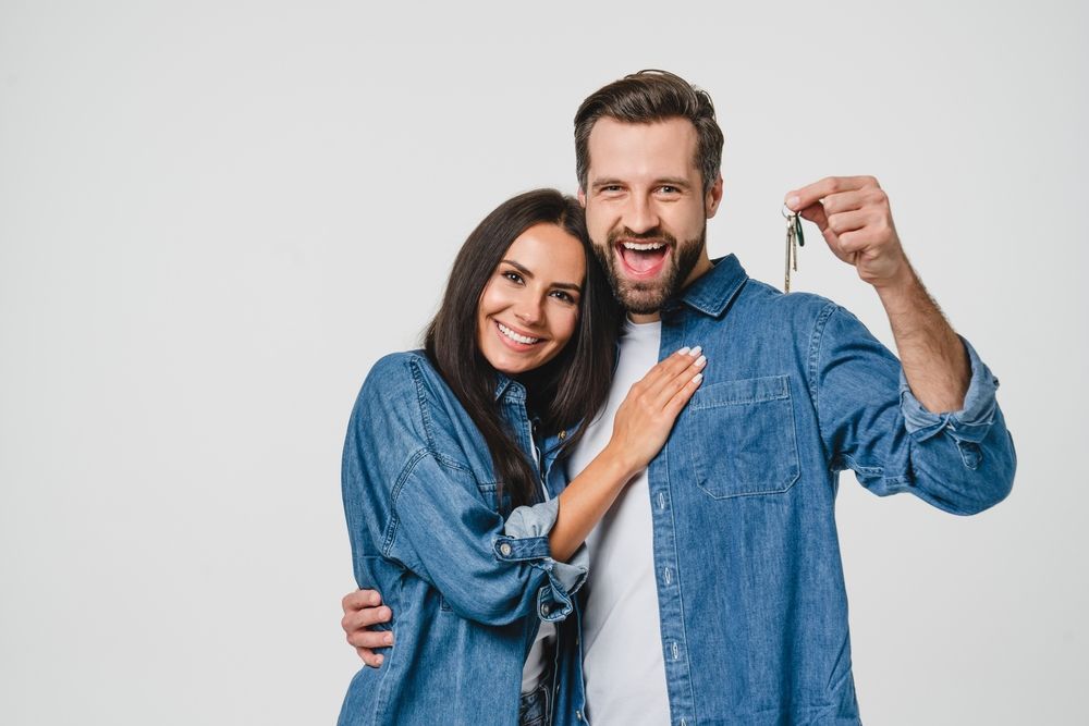 A man and a woman are standing next to each other holding keys to their new home.