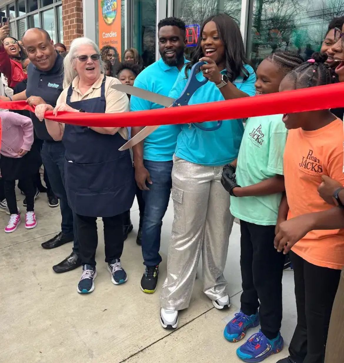 A group of people are cutting a red ribbon in front of an ice cream shop.