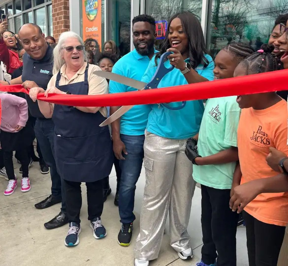 A group of people are cutting a red ribbon in front of an ice cream shop.