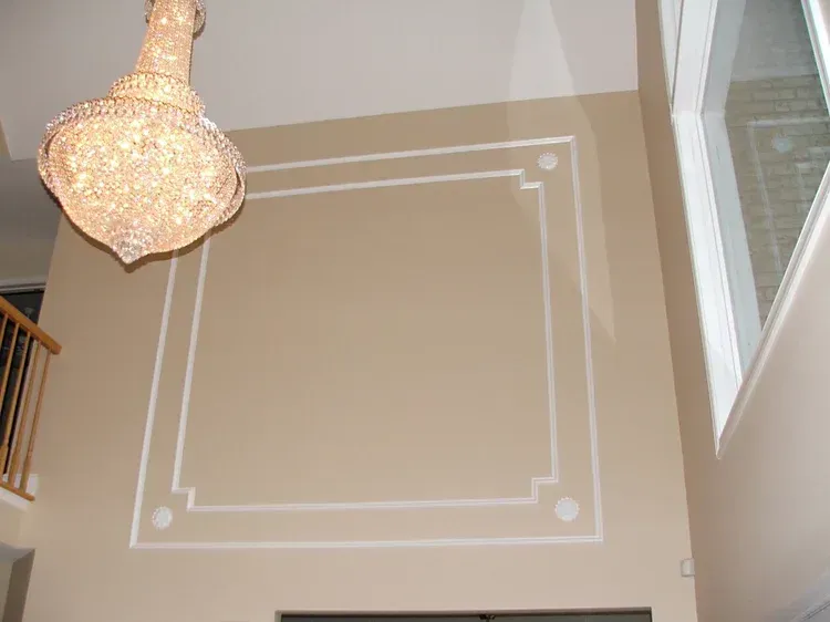 Beige wall with white decorative square molding; chandelier hangs above.