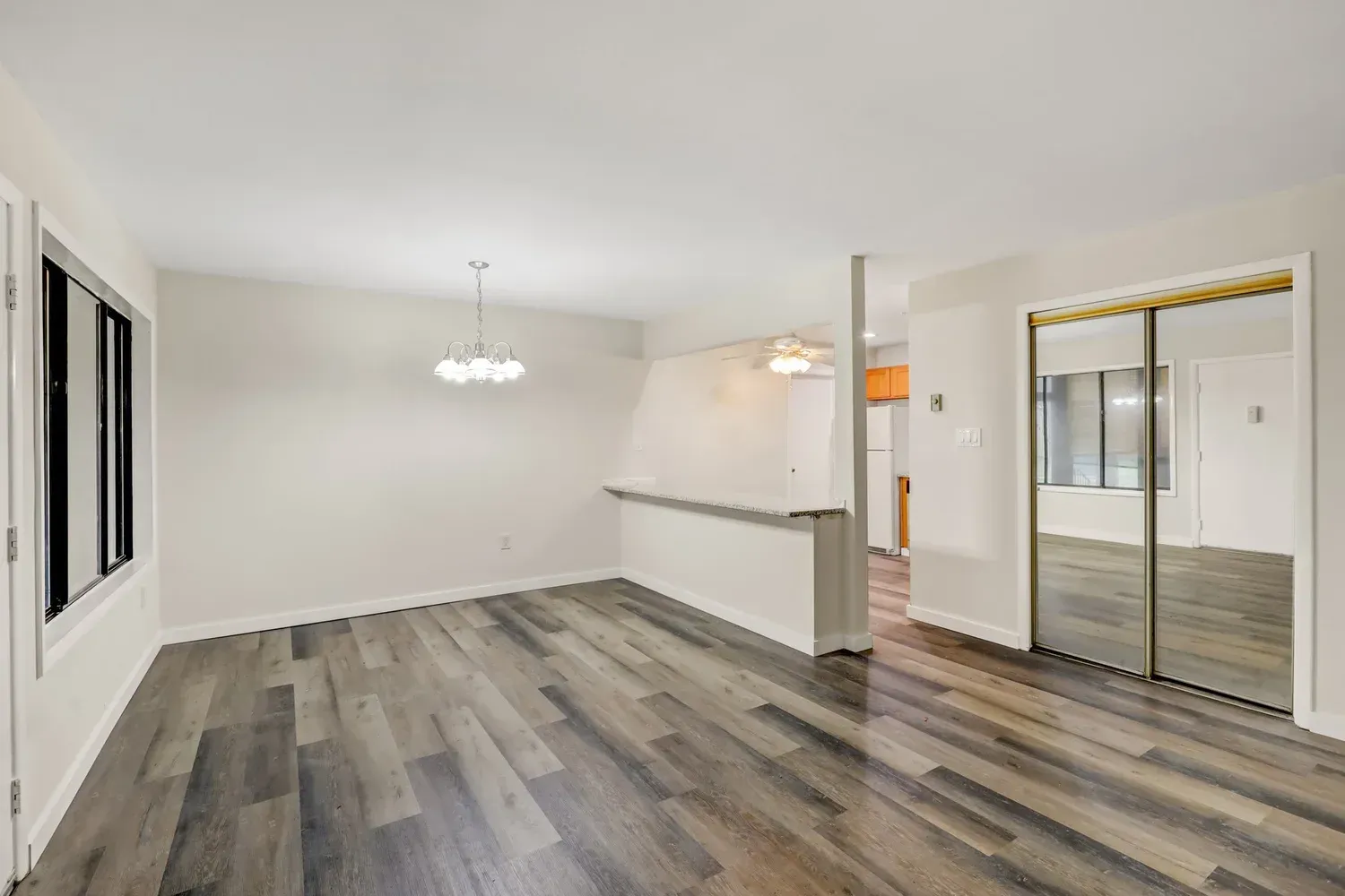 Empty living room with gray wood-look flooring, white walls, and a large mirrored closet door.