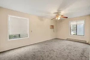 Empty room with gray carpet, two windows with shades, and ceiling fan.