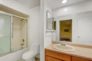 Bathroom with a white toilet, shower/tub combo, vanity, and mirror. Beige countertop and wood cabinet.