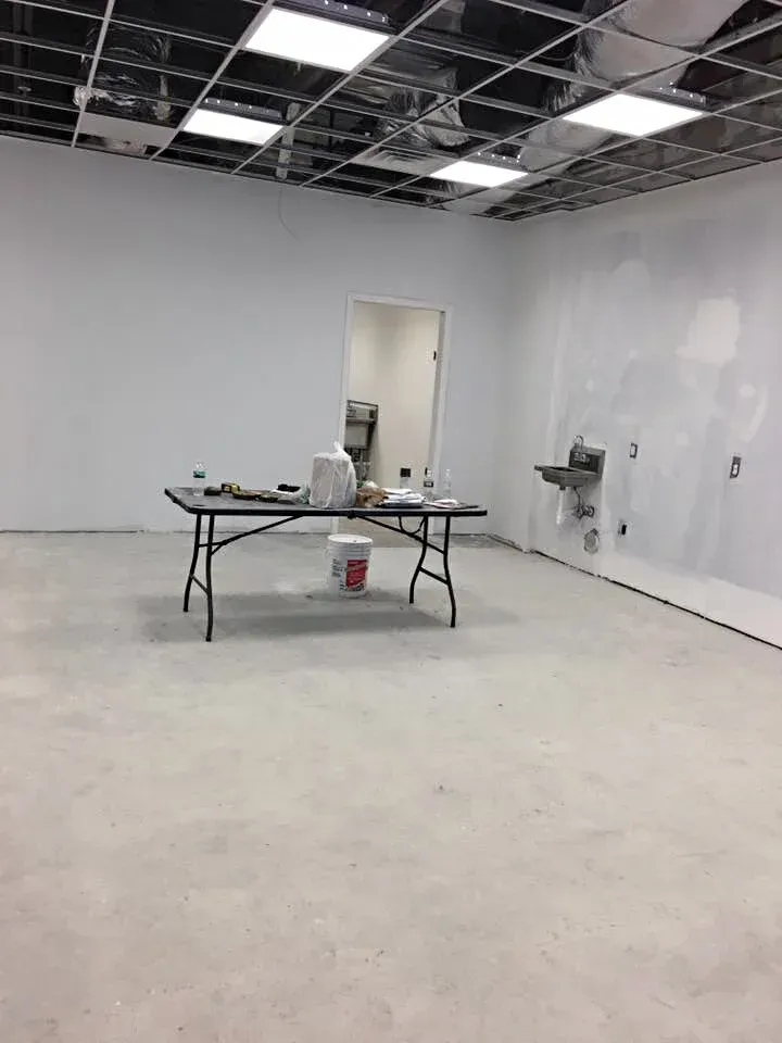 Empty room under construction with a folding table holding tools. White walls, unfinished ceiling, and concrete floor.