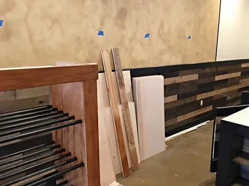 Construction site: Wood planks leaning against a white panel near a dark wood paneled wall and a wooden shelf structure.