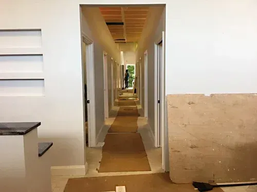 Long hallway with multiple doorways and construction materials on the floor and walls.