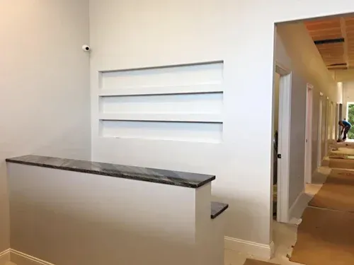 White wall with built-in shelves. Granite-topped counter and hallway with doors.
