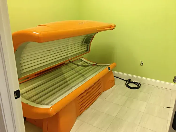 Orange tanning bed in a room with lime green walls and white tile flooring.