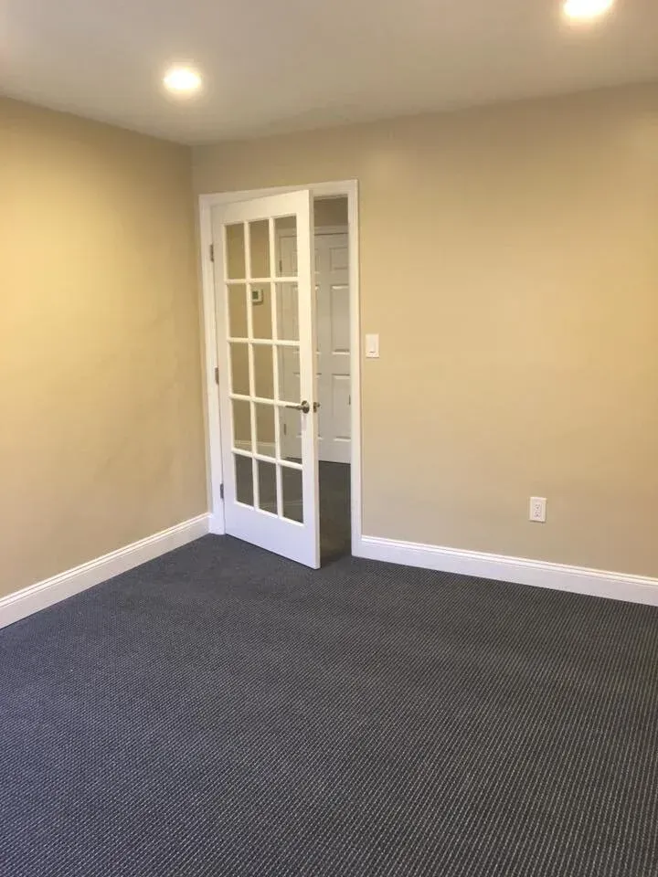 Empty room with beige walls, blue carpet, and a white, glass-paneled door.