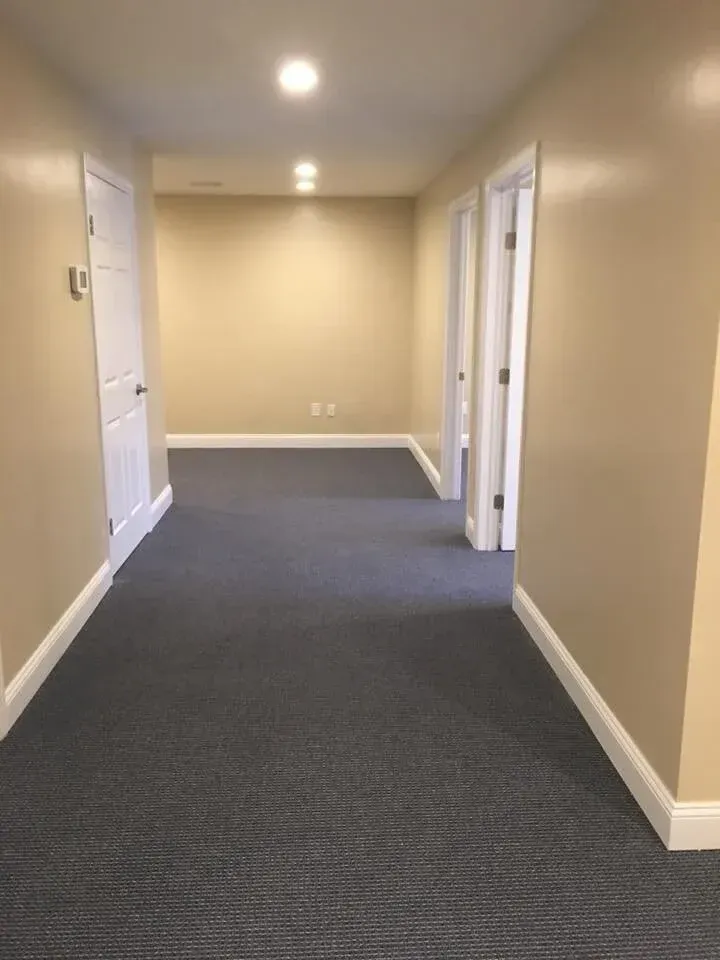 Long hallway with beige walls, white doors, and gray carpet.