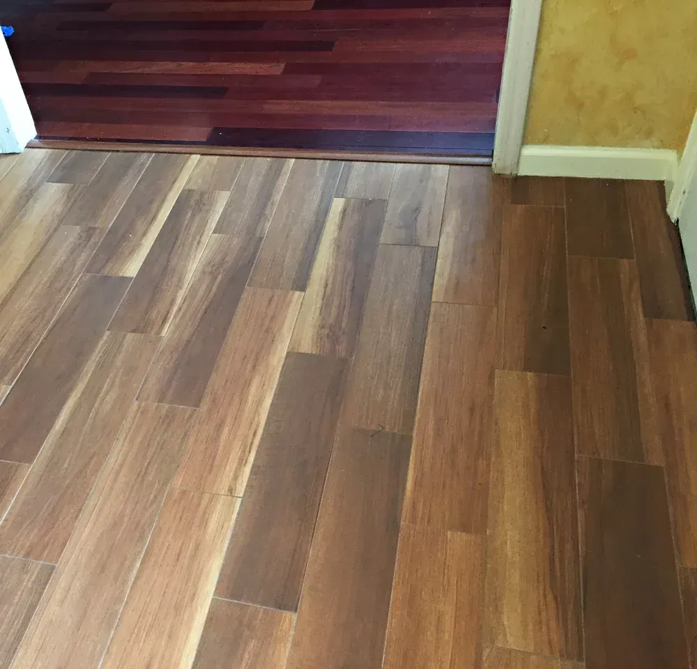 Wooden floors in a room, with different colored wood leading to a door.
