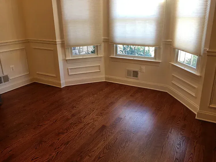 Empty room with hardwood floors, three windows with blinds, and white trim.